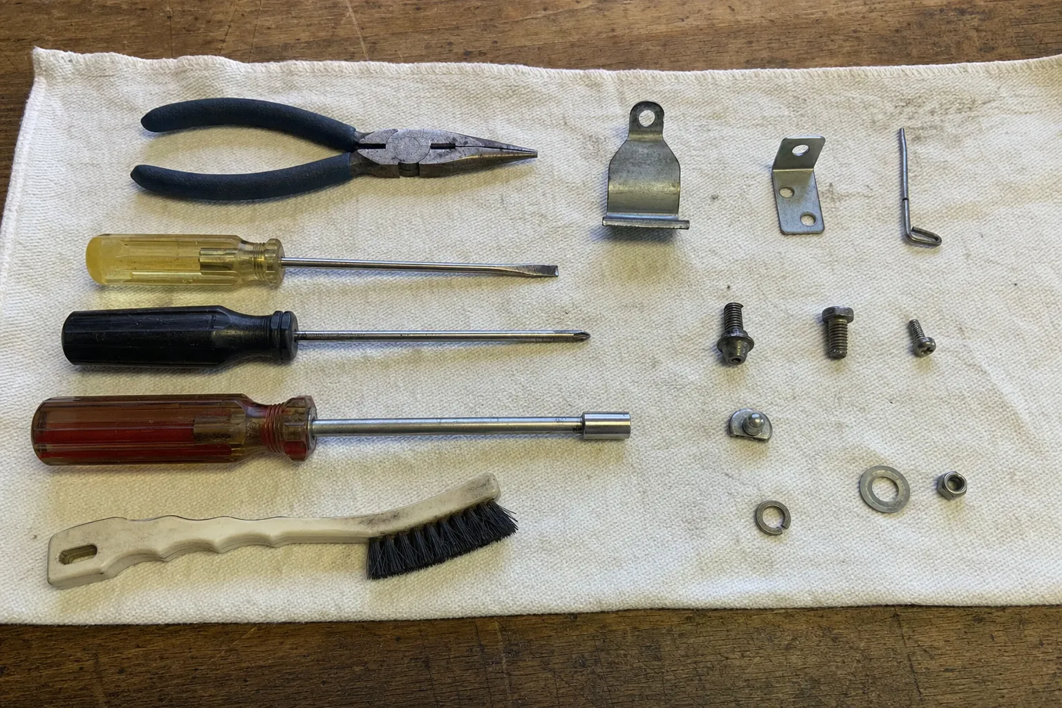 Hand tools, a stainless bracket and replacement fixings arranged on a cloth before a refrigerator repair