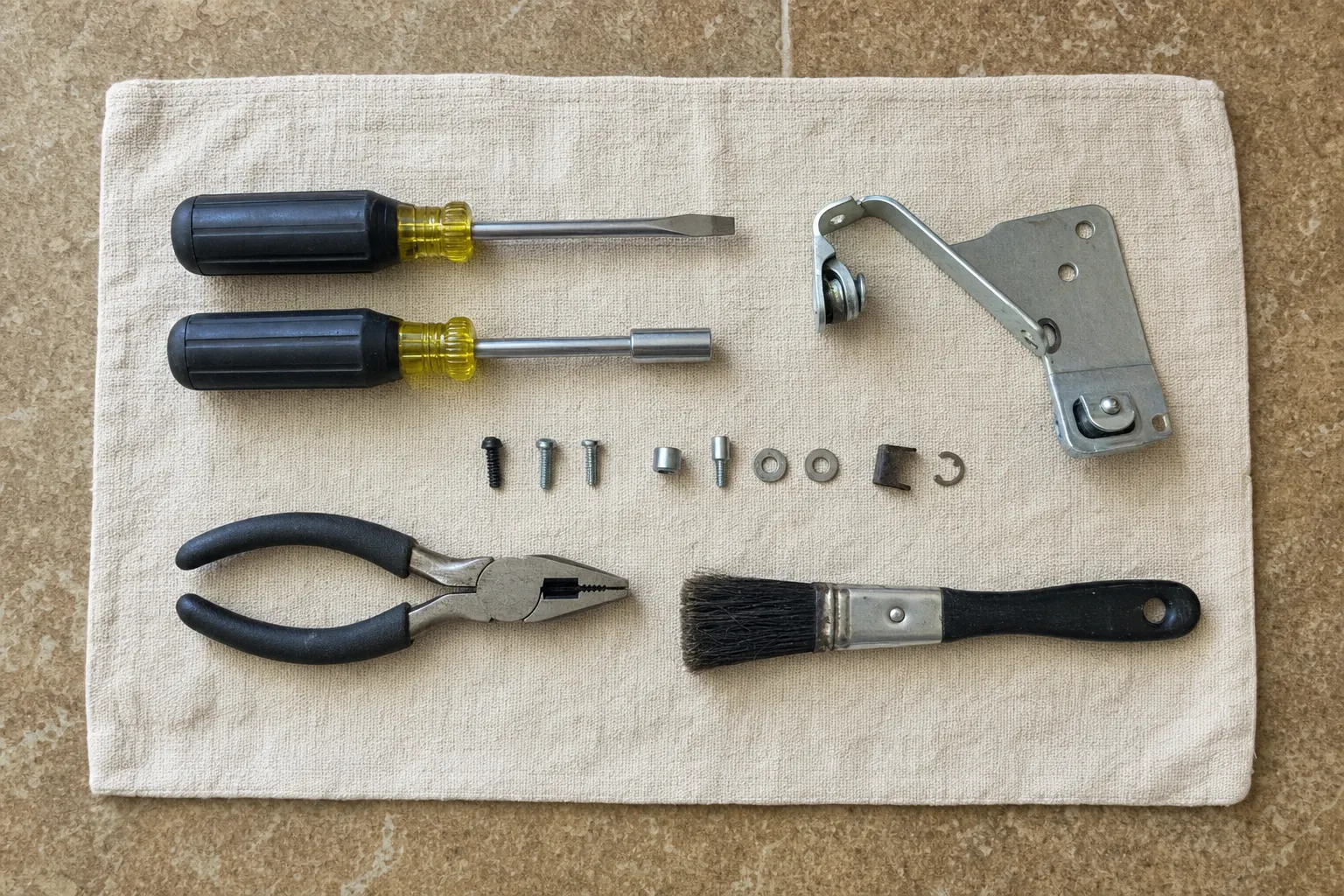 Nut drivers, combination pliers, a parts brush and a hinge bracket laid out on a cloth